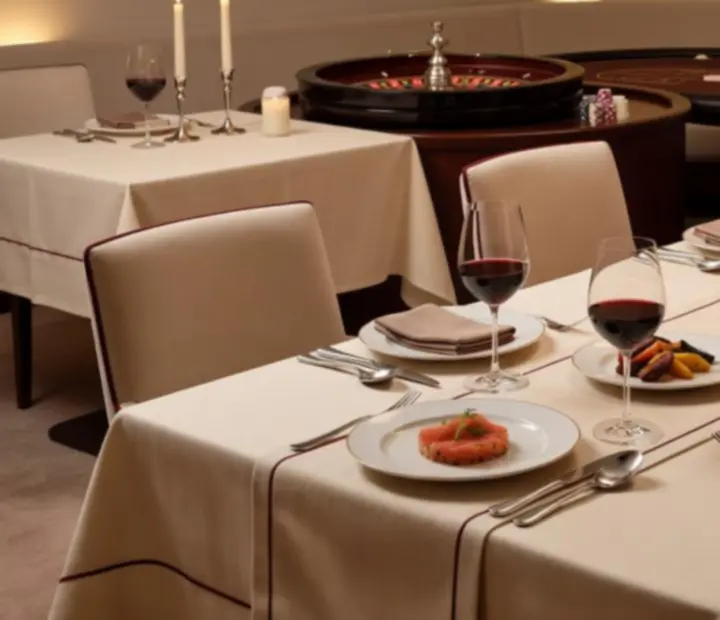 Kremowo urządzone stoły restauracyjne Savory Room Co z zastawą, winem i w oddali subtelną strefą kasyna z ruletką i pokerowym stołem