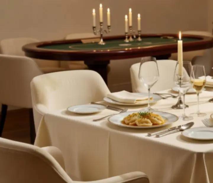 Elegancko nakryty kremowy stół w restauracji z kieliszkami wina, autorskimi daniami i dyskretnym pokerowym stołem w tle.